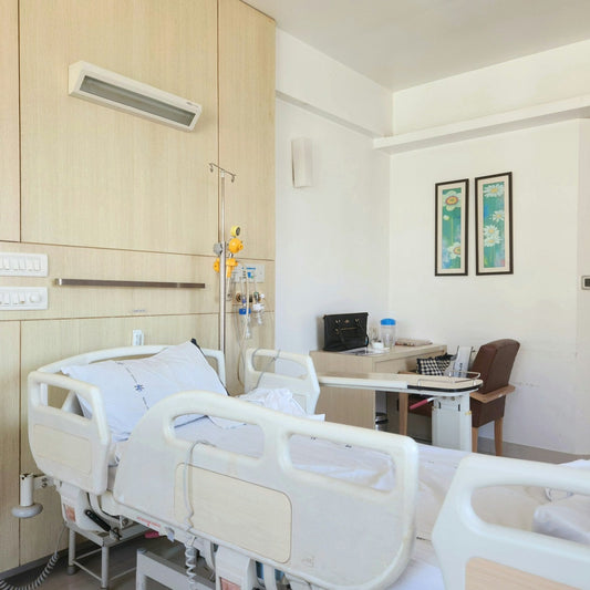 A calm, light-filled private hospital room with a neatly made bed, a chair and framed botanical prints on the wall