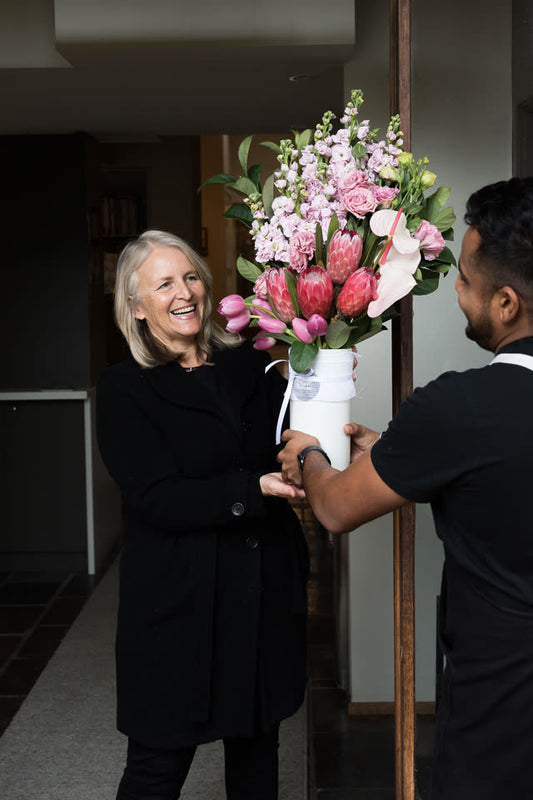 A Fig & Bloom arrangement being handed over at an office entrance, the recipient mid-smile