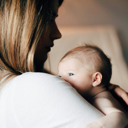A mother holding her newborn against her shoulder in soft window light