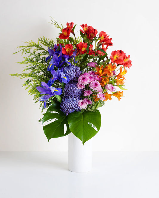 A vibrant mixed arrangement of colourful seasonal flowers in a white vase
