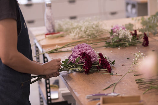 Hands holding flower stems at a wooden studio bench, face out of frame