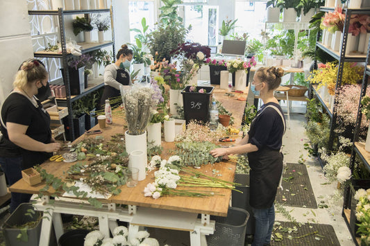 Three florists at a wooden studio workbench preparing eucalyptus and flowers in a bright Fig & Bloom studio