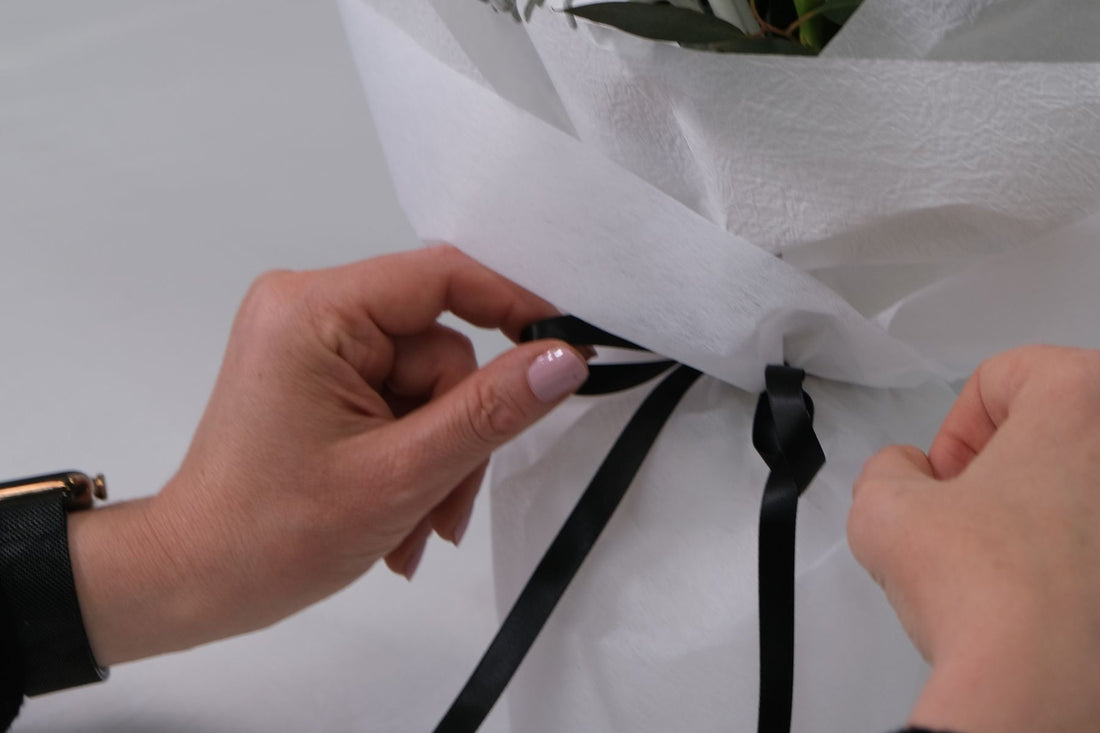 Hands tying a black ribbon around a white wrapped bunch