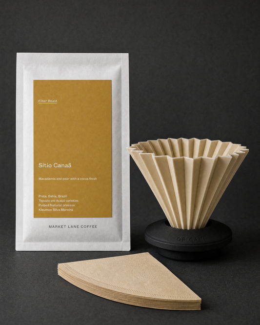 The Filter Ritual pour-over gift set on charcoal: Origami Air dripper in matte beige seated in the black AS holder, natural cone filters and a 250g bag of Market Lane Sitio Canaa filter coffee.