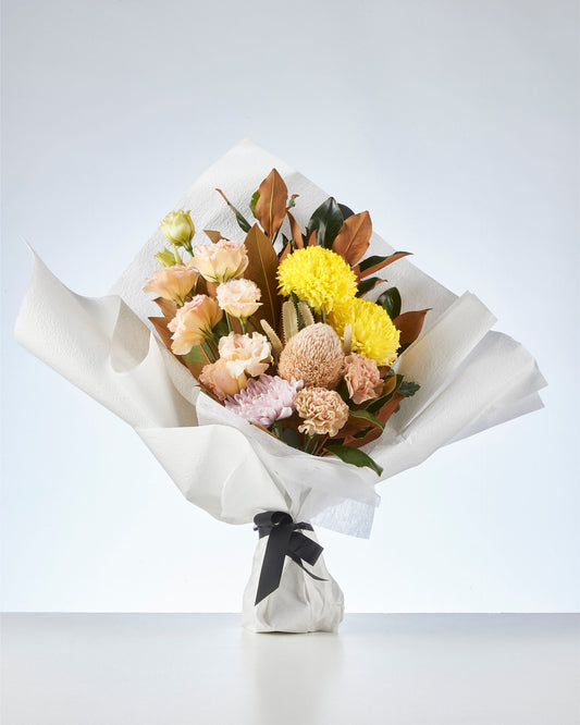 Umbria bouquet in yellow and peach, hand-wrapped in white paper with a black ribbon