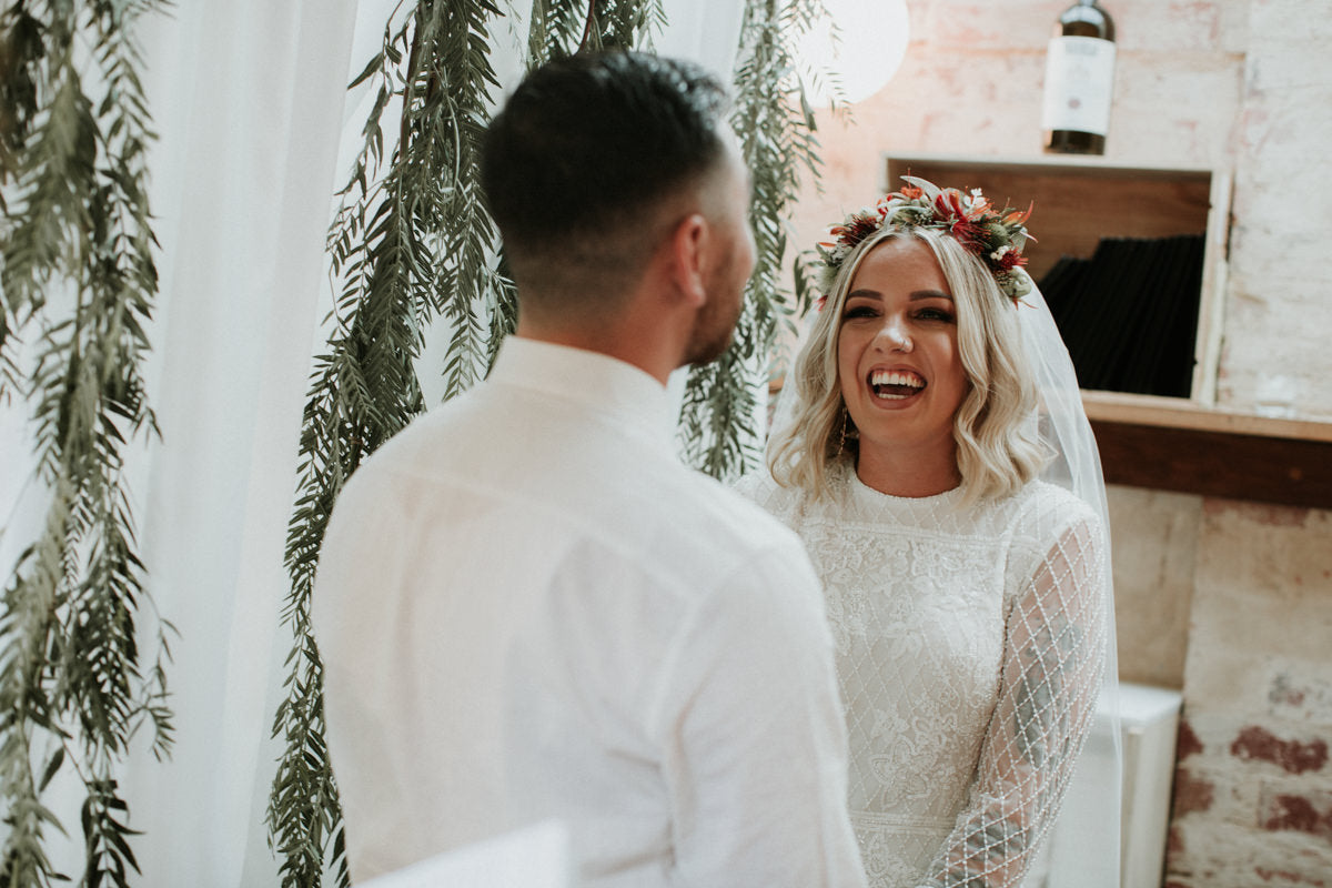 Bride in a red and native floral crown laughing during her ceremony at Cru wine bar, beneath hanging eucalyptus garlands by Fig & Bloom