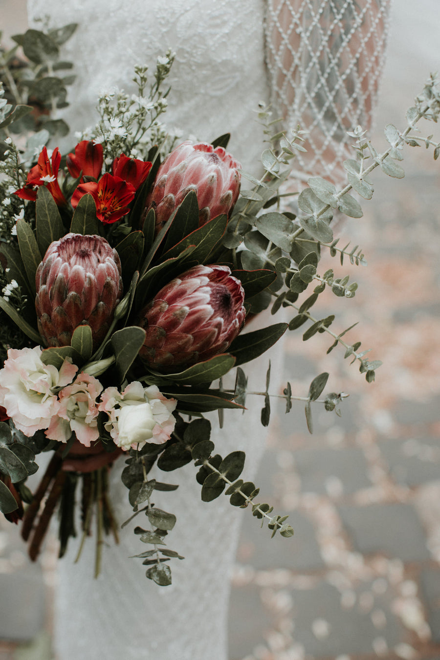 Bridal bouquet of pink king proteas, red alstroemeria, blush lisianthus and eucalyptus by Fig & Bloom
