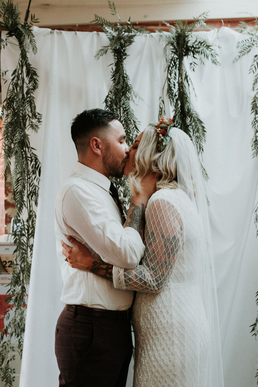 Bride and groom kiss in front of a white drape hung with eucalyptus garlands at Cru