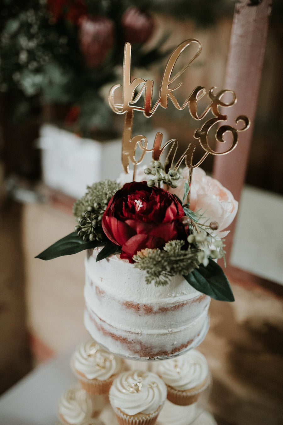 Naked wedding cake topped with a deep red bloom and native foliage