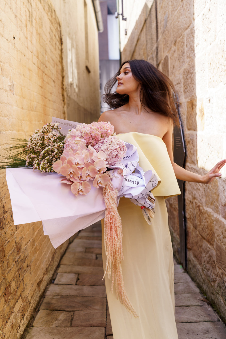 Model in a pale yellow gown holding the Carmen arrangement in a sandstone laneway