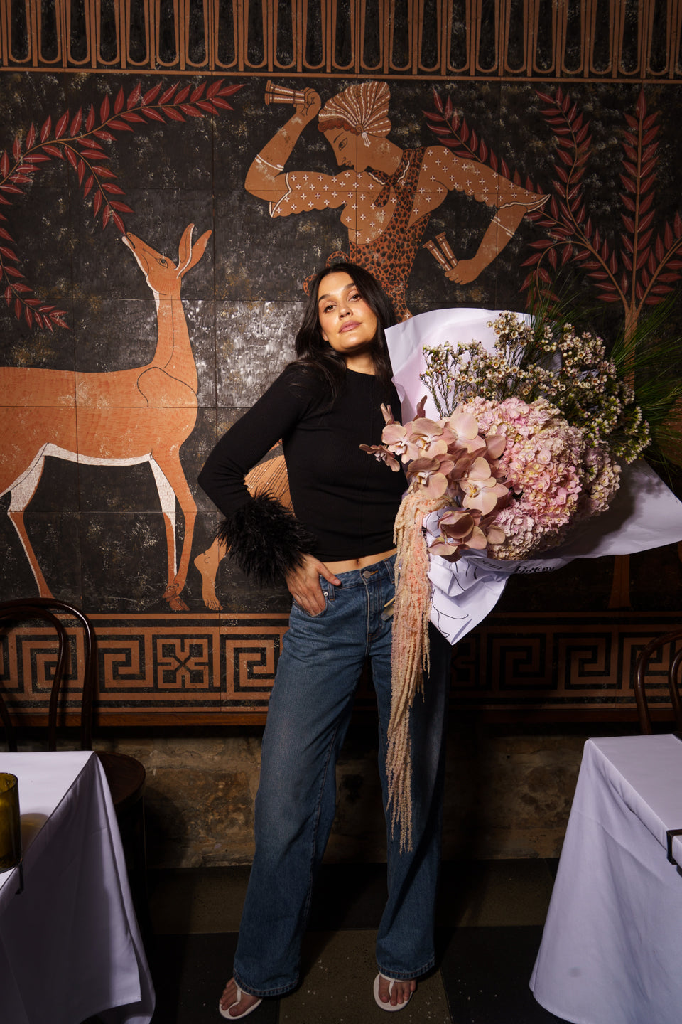 Model in black knit and jeans holding the Carmen arrangement in front of a painted mural