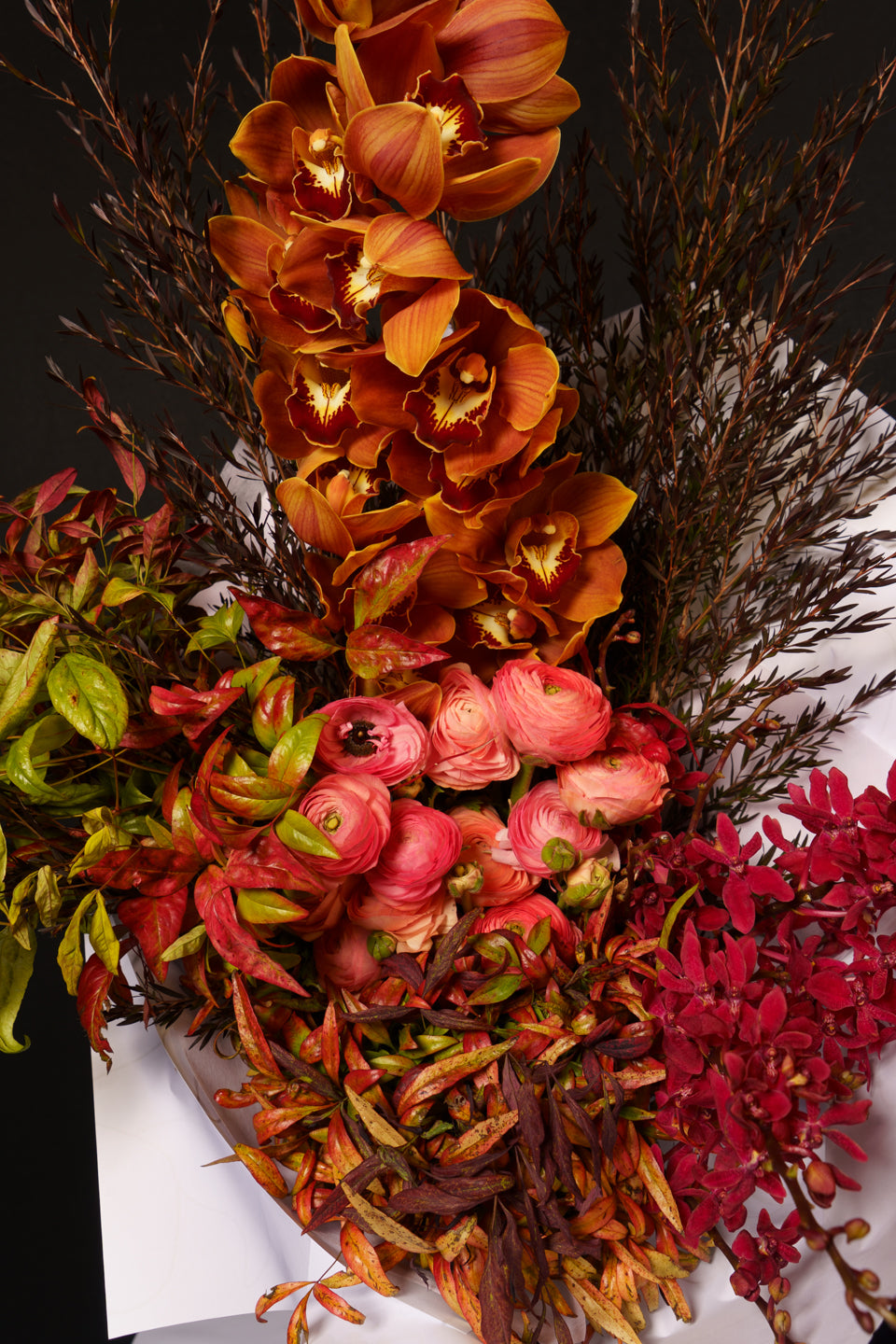 Close detail of the Sienna arrangement: rust orchids, coral peonies and red blooms