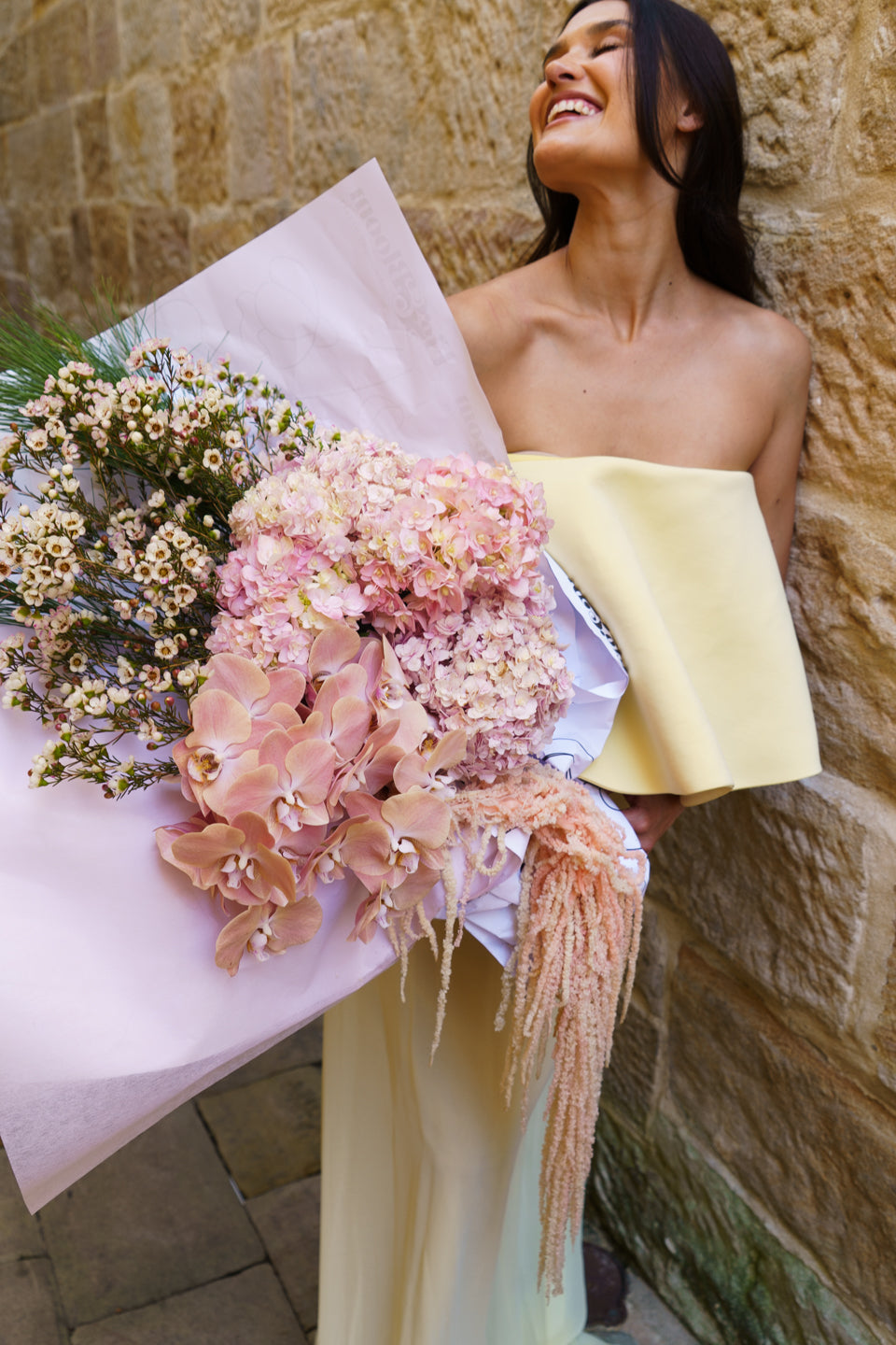 Model in pale yellow smiling over the Carmen arrangement in a sandstone laneway