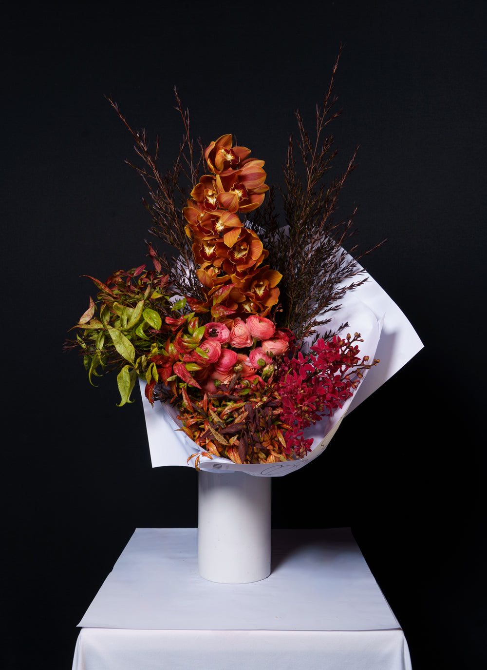 Sienna arrangement of rust and terracotta blooms in copper beech on a white plinth against black