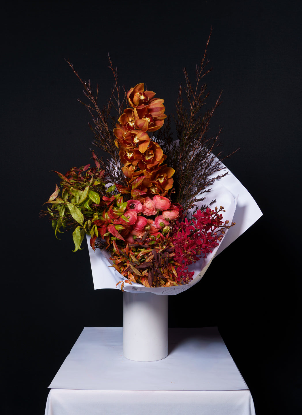 Sienna arrangement of rust and terracotta blooms in copper beech on a white plinth against black