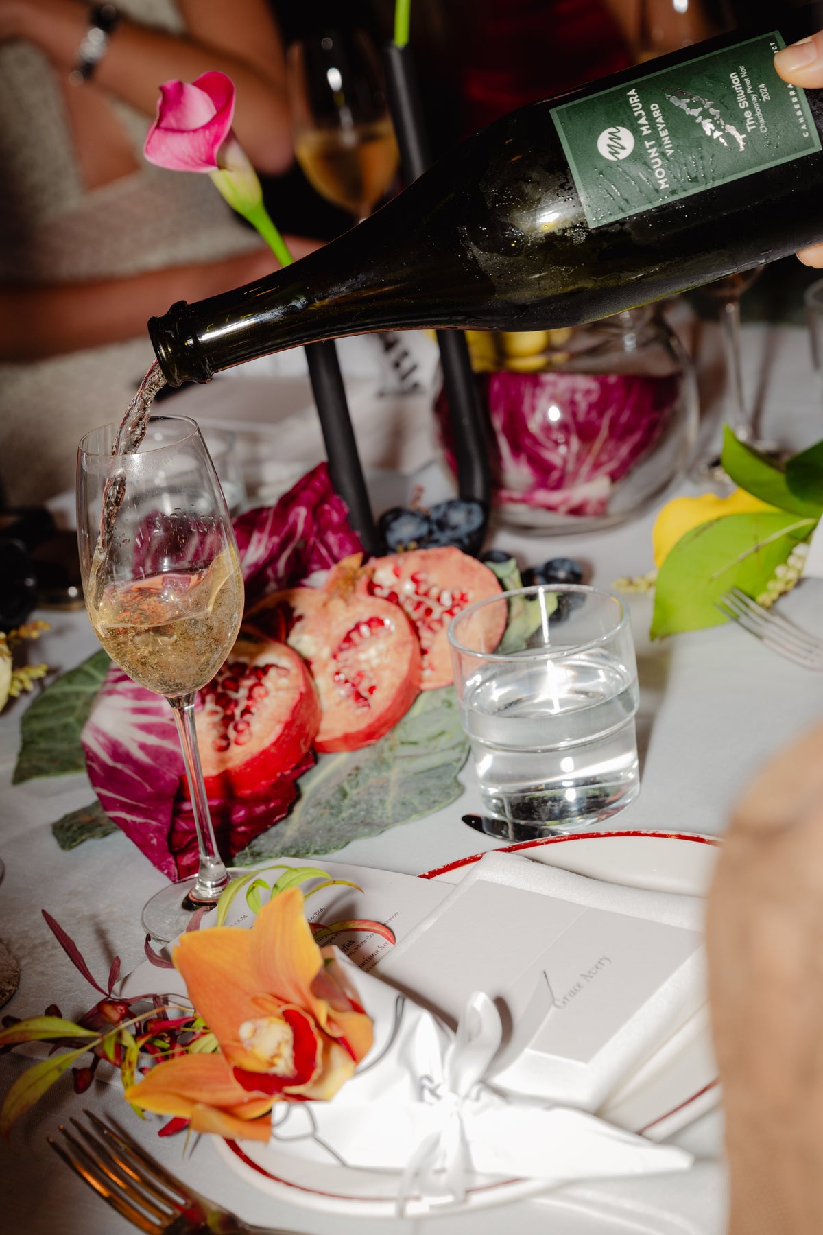 Wine poured over table florals of pomegranate, calla and orchid