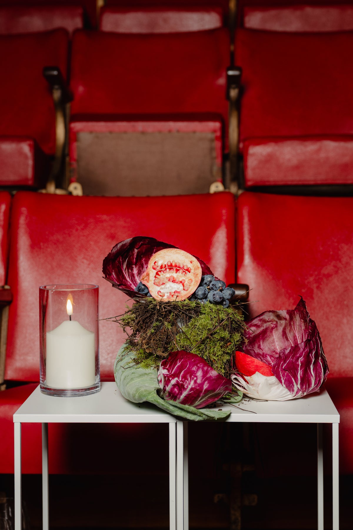 Floral still life of pomegranate and radicchio on a white stand among red theatre seats
