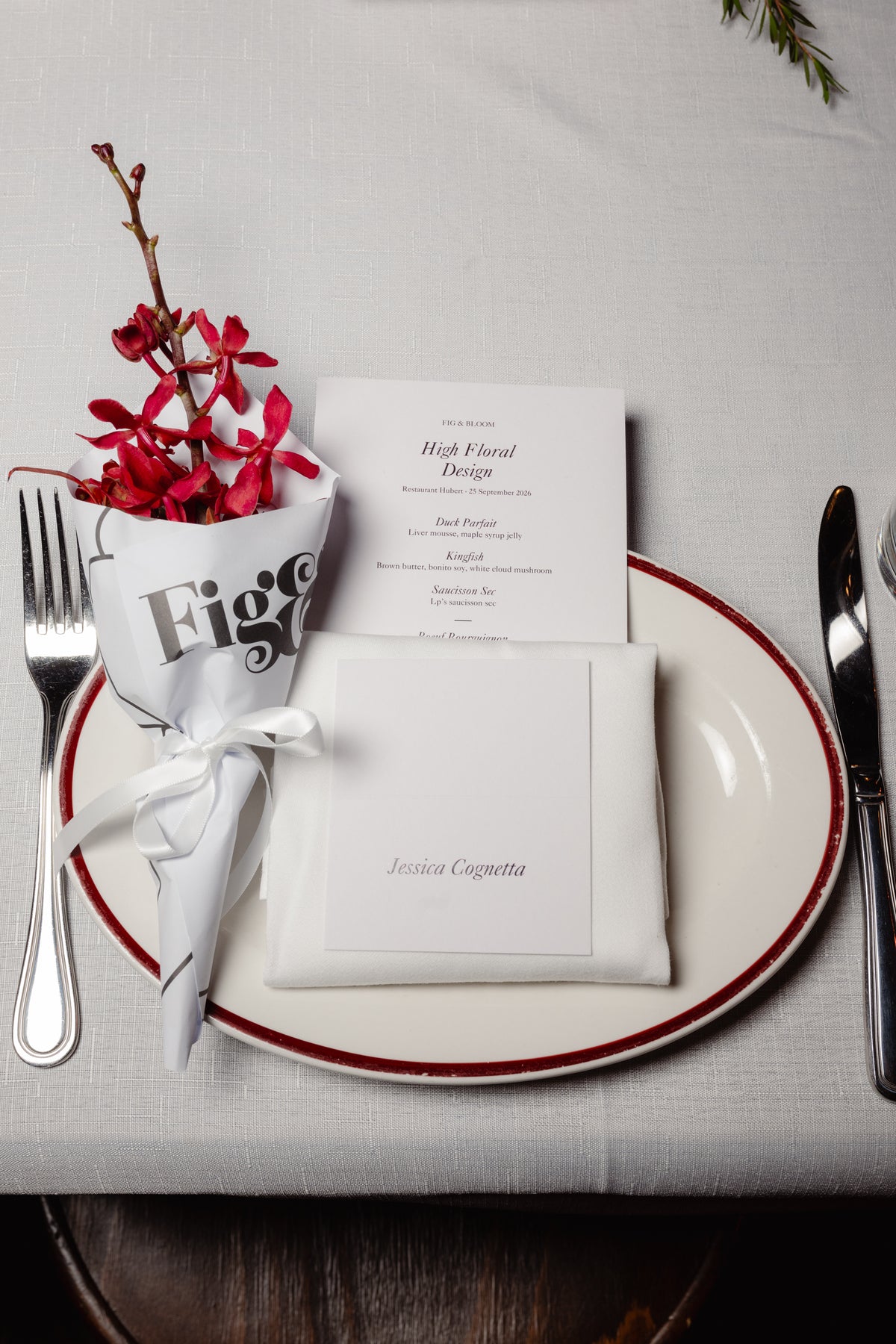 Place setting with a wrapped posy, menu and name card on a red-rimmed plate