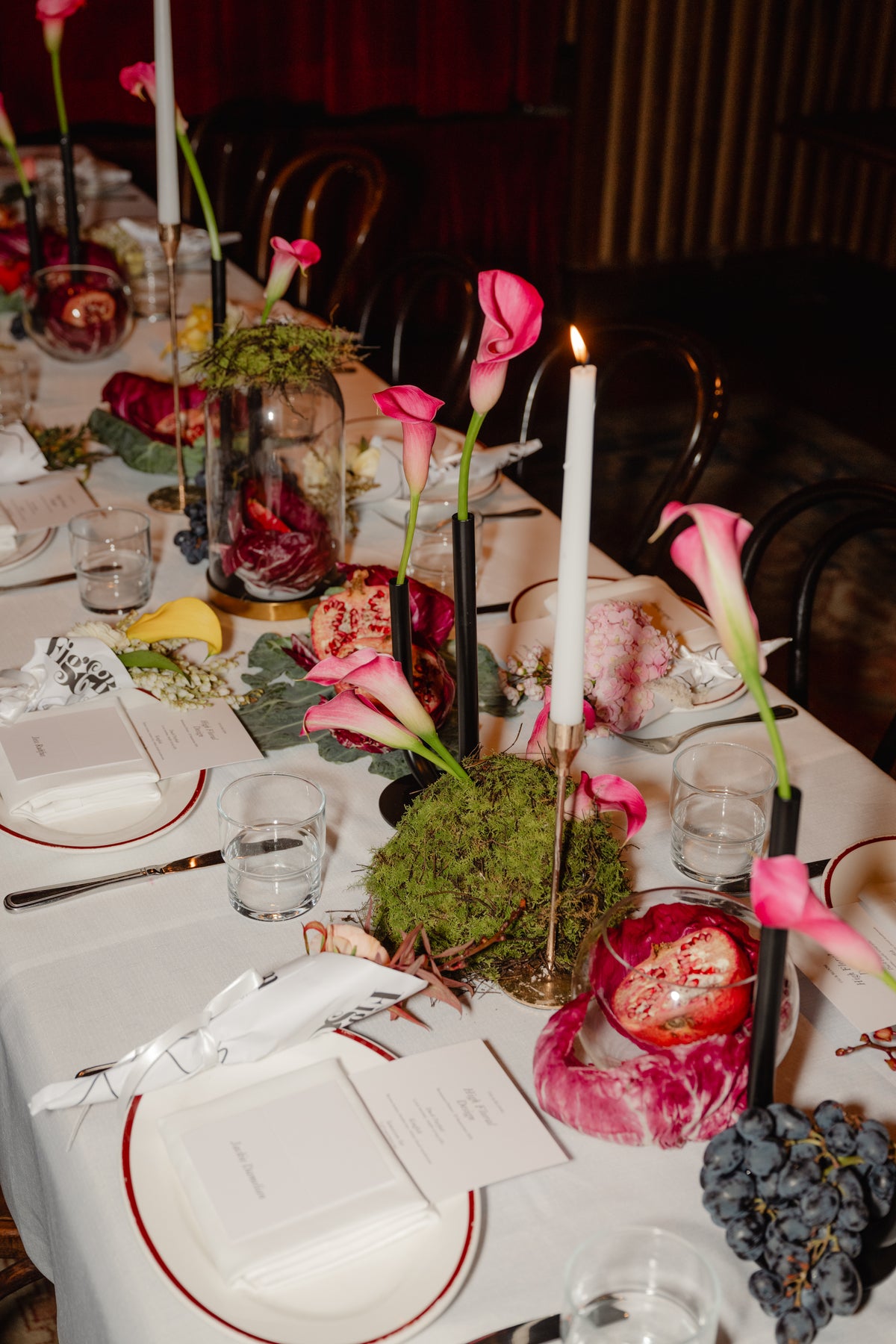 Table centrepiece of moss, pomegranate, radicchio and pink calla lilies with taper candles