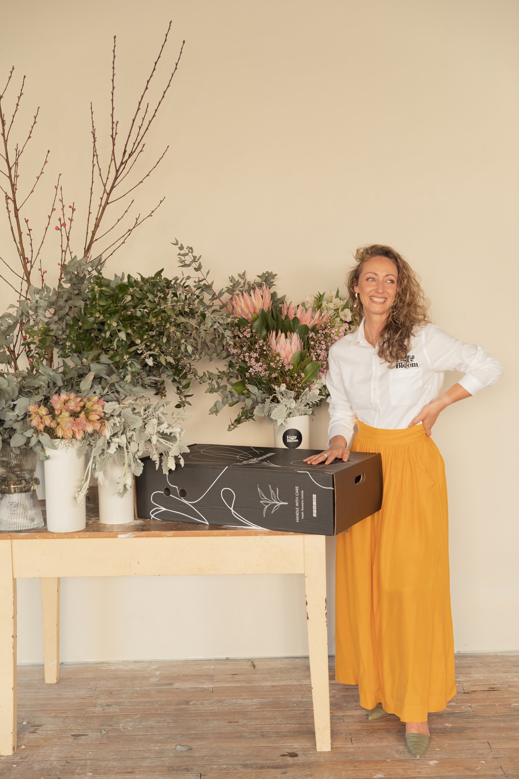 Kellie Brown, founder of Fig & Bloom, standing beside a black Fig & Bloom flower box on a studio bench
