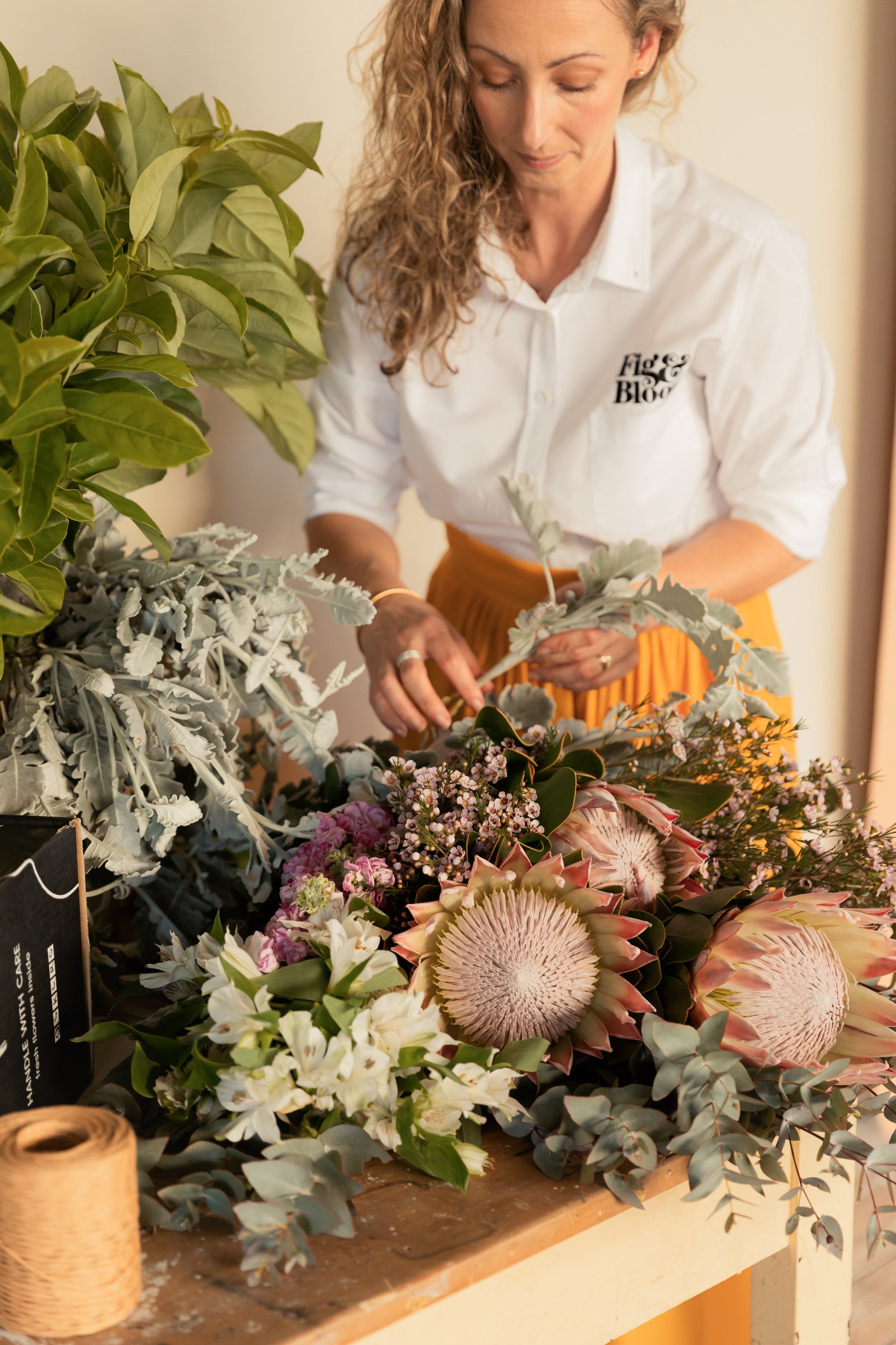 Kellie Brown arranging dusty miller, king proteas and alstroemeria on the studio bench