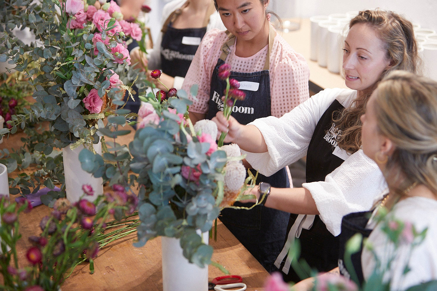Kellie Brown guiding a participant's hands while arranging roses and eucalyptus