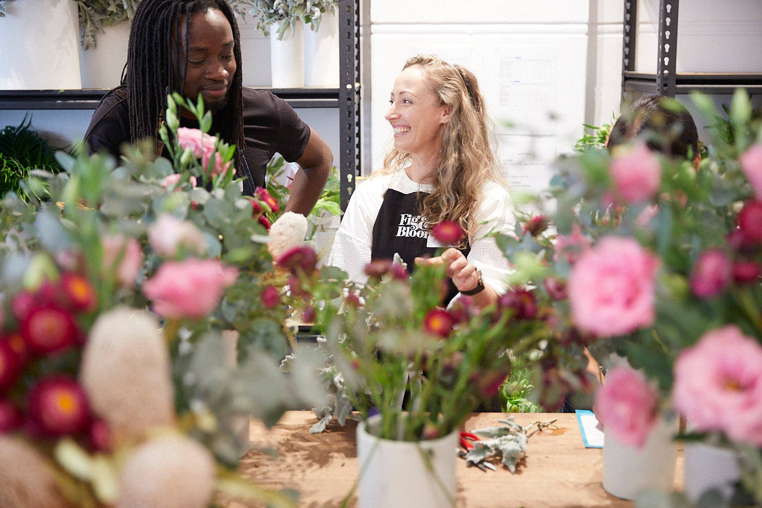 Kellie Brown and a participant laughing behind a bench of pink and burgundy blooms