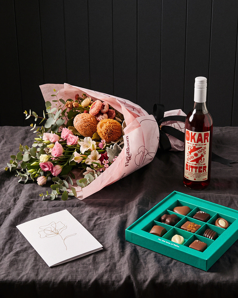 The Aperitif gift set laid on charcoal linen with Okar Bitter, chocolates and the Single Stem greeting card