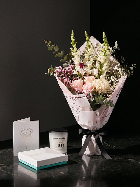 The Fuss, the Osaka Gesture bouquet tied with black ribbon on dark stone, with the Fig & Olive Leaf candle, Koko Black chocolates and the greeting card.