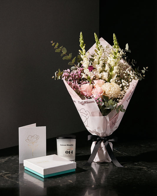 The Fuss, the Osaka Gesture bouquet tied with black ribbon on dark stone, with the Fig & Olive Leaf candle, Koko Black chocolates and the greeting card.