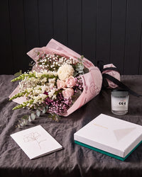 The Fuss resting on charcoal linen in window light, with the candle, chocolates and greeting card alongside.