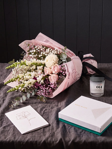 The Fuss resting on charcoal linen in window light, with the candle, chocolates and greeting card alongside.