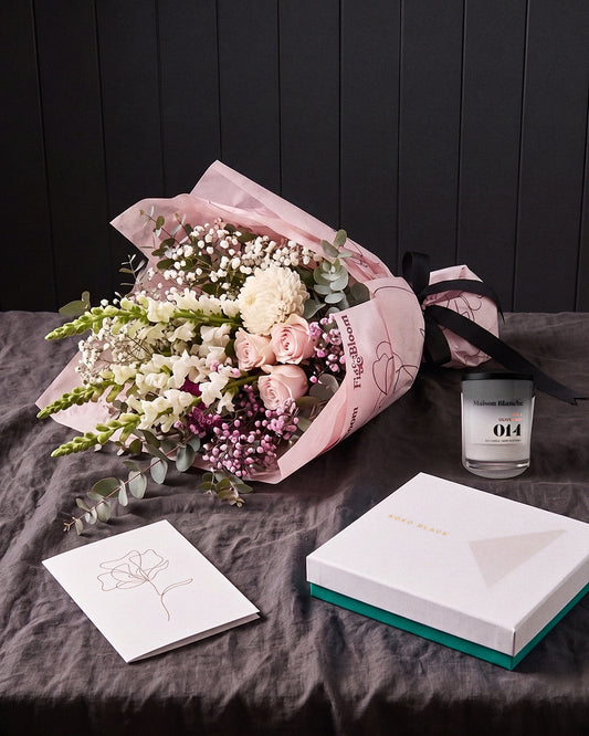 The Fuss resting on charcoal linen in window light, with the candle, chocolates and greeting card alongside.