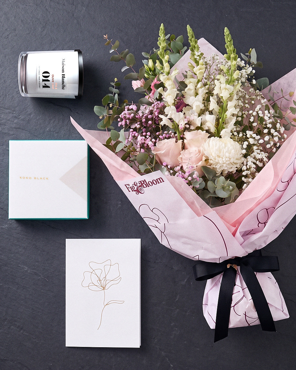 The Fuss photographed from above on charcoal slate: the Osaka Gesture bouquet, candle, Koko Black chocolates and greeting card.