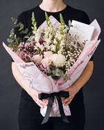 The Fuss, the Osaka Gesture bouquet held at chest height with the greeting card tucked into the wrap, against a charcoal backdrop.