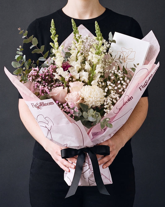 The Fuss, the Osaka Gesture bouquet held at chest height with the greeting card tucked into the wrap, against a charcoal backdrop.