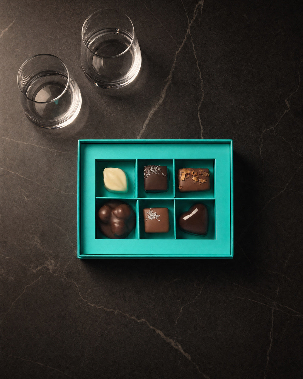 Koko Black Chocolatier's Selection six-piece box open beside the pair of tumblers, from above on charcoal