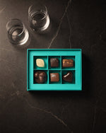 Koko Black Chocolatier's Selection six-piece box open beside the pair of tumblers, from above on charcoal