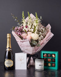 The Lot, the Osaka bouquet tied with black ribbon on dark stone, with House of Arras Brut Elite, the Koko Black nine-piece selection, the Fig & Olive Leaf candle and the greeting card.