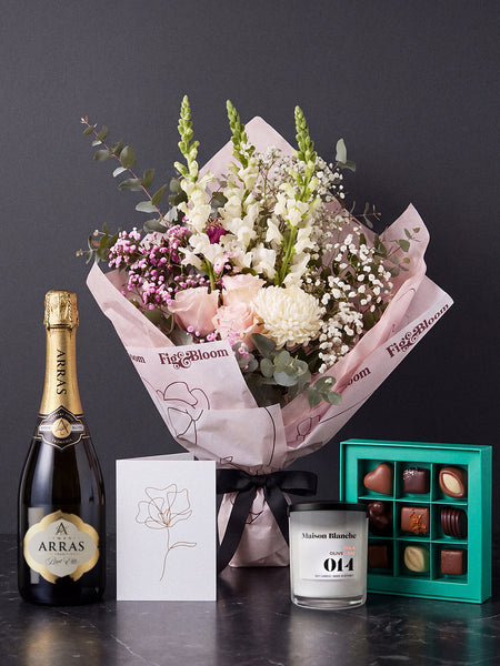 The Lot, the Osaka bouquet tied with black ribbon on dark stone, with House of Arras Brut Elite, the Koko Black nine-piece selection, the Fig & Olive Leaf candle and the greeting card.
