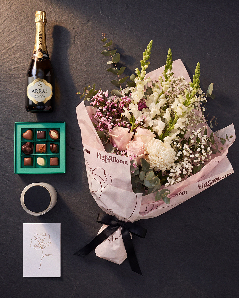 The Lot photographed from above on charcoal slate: the Osaka bouquet, House of Arras, Koko Black chocolates, the candle and the greeting card.