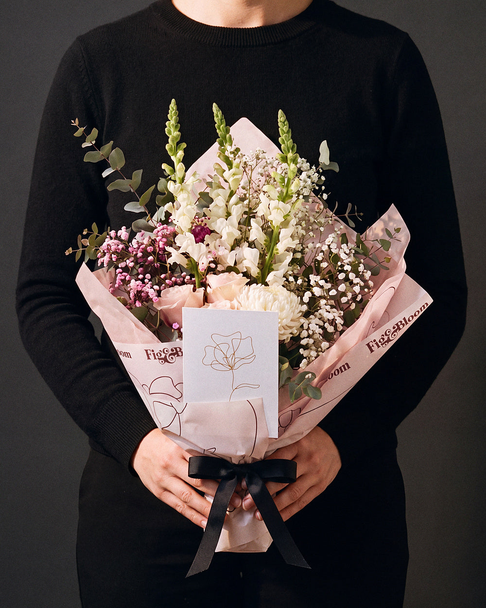 The Lot, the Osaka bouquet held at chest height with the greeting card tucked into the wrap, against a charcoal backdrop.