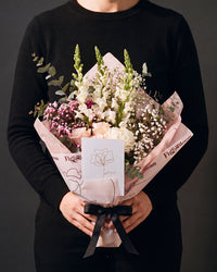 The Lot, the Osaka bouquet held at chest height with the greeting card tucked into the wrap, against a charcoal backdrop.