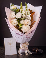 The Toast, the Pyrenees Gesture bouquet with a greeting card and a plate of dark chocolate marbles, on dark stone.