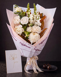The Toast, the Pyrenees Gesture bouquet with a greeting card and a plate of dark chocolate marbles, on dark stone.