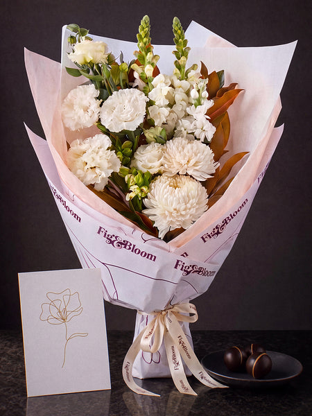 The Toast, the Pyrenees Gesture bouquet with a greeting card and a plate of dark chocolate marbles, on dark stone.