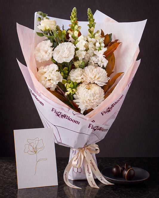 The Toast, the Pyrenees Gesture bouquet with a greeting card and a plate of dark chocolate marbles, on dark stone.