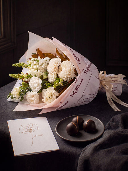 The Toast, the Pyrenees Gesture bouquet resting on charcoal linen in window light, with the greeting card and dark chocolate marbles.
