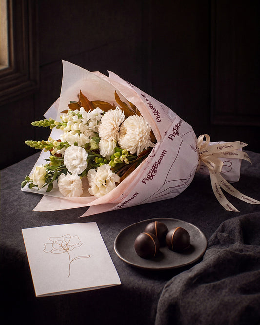 The Toast, the Pyrenees Gesture bouquet resting on charcoal linen in window light, with the greeting card and dark chocolate marbles.