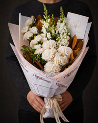 The Toast, the Pyrenees bouquet held at chest height with the greeting card tucked into the wrap, against a charcoal backdrop.